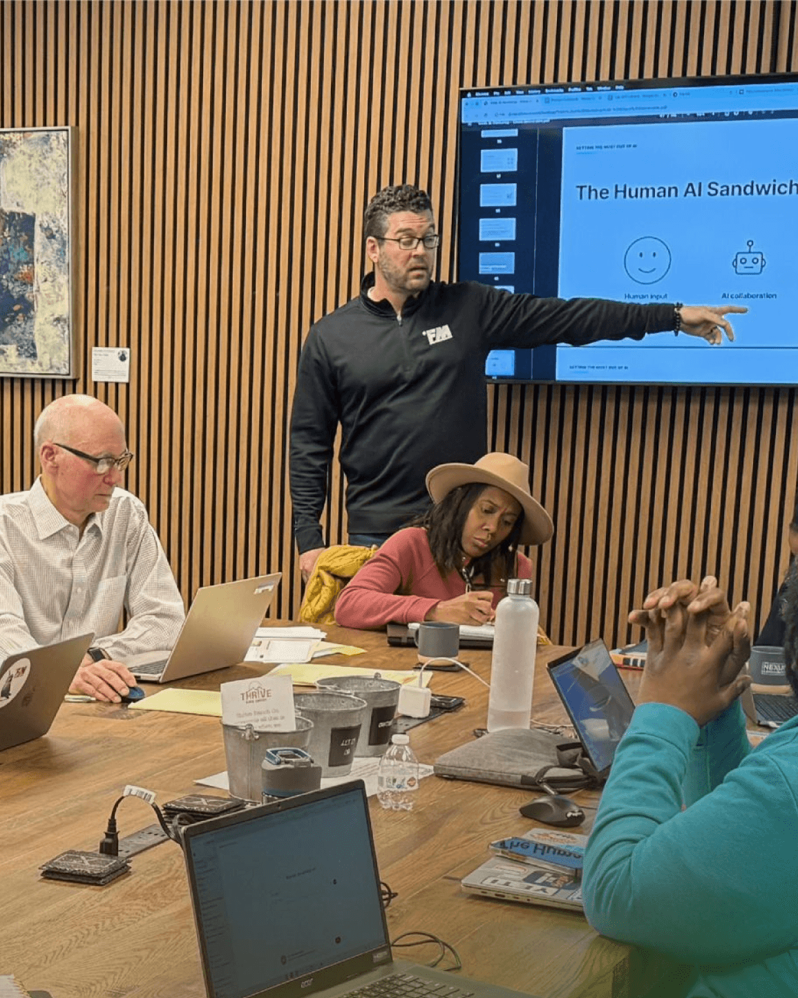 An FM Labs workshop in progress: participants working on laptops around a conference table while Tim Visconti presents at a screen.